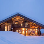 Éclairage de nuit d'un chalet renforçant le côté féérique du contraste entre habitation et neige.