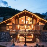 chalet illuminé de nuit avec de grandes baies vitrées et une hauteur sous plafond.