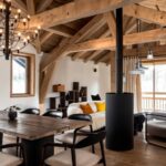 Vaste salon en bois dans une ambiance chaleureuse et lumineuse, composé d'un poêle à bois central , d'une grande table et de canapés cosy.