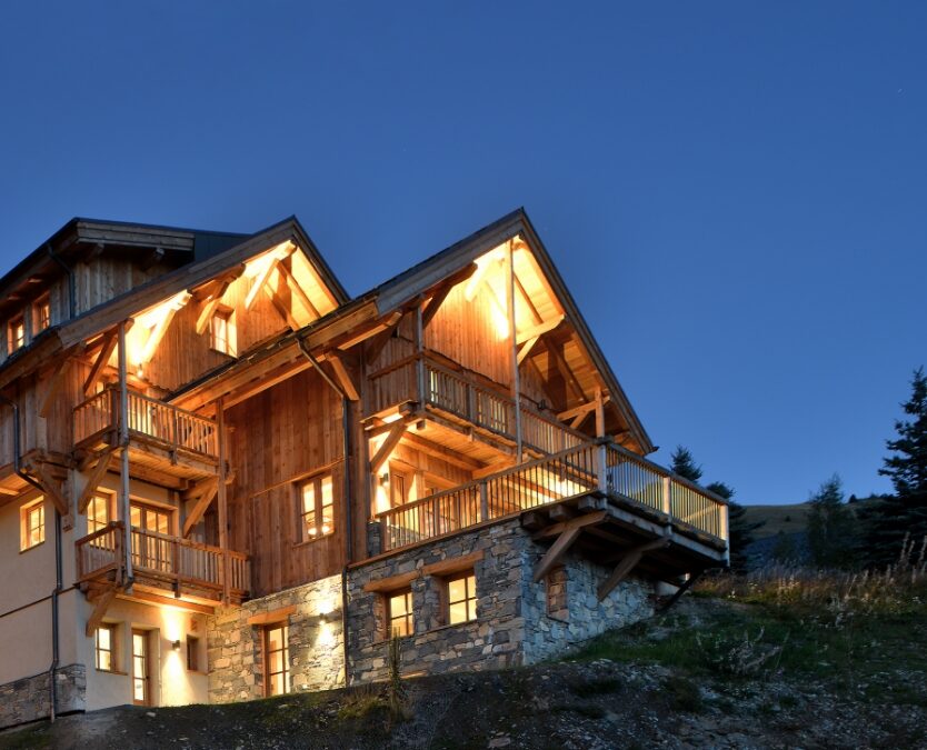 Vue saisissante du chalet tout éclairé de nuit qui met en valeur l'architecture.