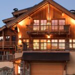 Vue de face d'un chalet illuminé ADVP, mise en valeur des 2 étages avec balcons et garage.