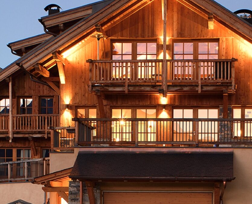 Vue de face d'un chalet illuminé ADVP, mise en valeur des 2 étages avec balcons et garage.