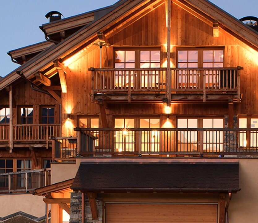 Vue de face d'un chalet illuminé ADVP, mise en valeur des 2 étages avec balcons et garage.